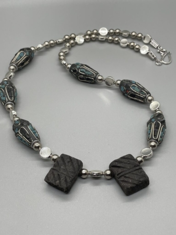 Unisex Neckwear- Round Silver Metal Balls. Silver Metal Rectangle Beads. Large Stone Covered with Turquoise and Grey Color Stone Chips Encased in Silver Metal. Grey Drop Clay-Double Sided Line Design Centerpiece. Approx. length: 23 inches. Pronounced: KEH-L-EH-N. Origin: Africa. Meaning: Powerful