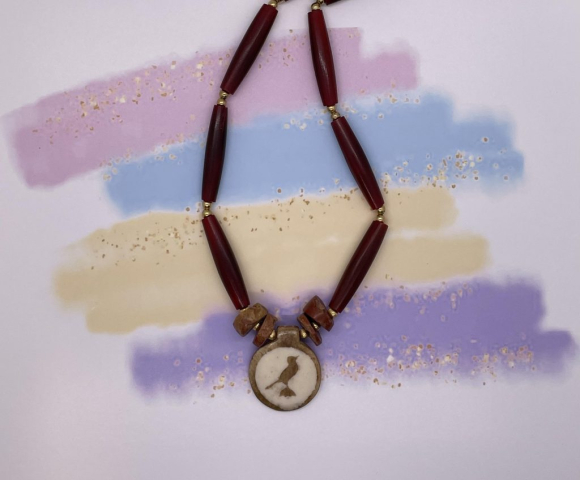 Unisex Neckwear- Long Red Horn Beads. Bauxite Stone Accents. Gold Metal Accents. Bone Shield Centerpiece. Approx. length: 21 inches. Pronounced: TAH-dah-lah Origin: Chewa Meaning: We Have Been Blessed