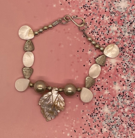 Ankle Bracelet- Silver Metal Beads. Teardrop and Oval Mother-of-Pearl Beads. Silver Metal Engraved Triangular Shaped Beads. Silver Metal Balls. Centerpiece: 1 1/4 inches. Mother-of-Pearl Leaf Cut Design. Approx. length: 9 inches Pronounced: A-be-bah Origin: Bembe Meaning: Surprisingly Useful