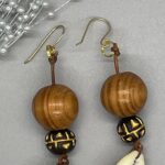Earrings- Pinewood Round Beads. Brown and Gold Clay Beads. Natural Cowrie Shells. Brown leather strung. Approx. length: 3 inches. Hand Shaped 14K Gold Filled Earwire. Pronounced: FAW-LAH-YAHN. Origin: Africa. Meaning: Walking Proud