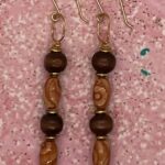 Earrings- Polished Wood Beads. Beige and Tan Cats Eye Wood Barrel Beads. Gold Metal Accents. Approx. length: 2 1/2 inches. 14K Gold Filled Earwire. Pronounced: YAH Origin: Western African Meaning: Born on Thursday