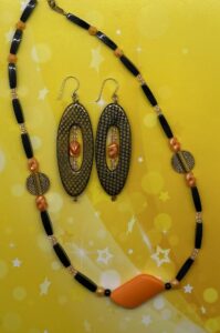 Necklace Set- Four Sided Acrylic Tube Beads. Bicone Beads. Translucent orange Lined Pony Beads. Fluted Orange Acrylic Beads. Gold Metal Carved Discs. Round Orange Acrylic Beads. Small Black Acrylic Beads. Trapezoid Pendant. Approx. length: 19 1/2 inches. 3 3/8 inch Earrings to Match. Snakeskin Pattern Oval Earrings. .925 Sterling Silver Earwire. Translucent orange Lined Pony Beads. Fluted Orange Acrylic Beads. 14K Gold Filled Earwire. Pronounced: boo-KEE-we. Origin: Xhosa. Meaning: Adorable