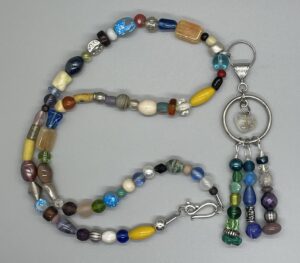 Necklace- Various Shaped Mixed Glass Metal, Stone, and Wood Beads. 5 inch Dangling Mixed Bead Centerpiece with Acrylic Heart. Approx. length: 23 inches. Pronounced: EE-KOO-SHE-HAN. Origin: Africa. Meaning: Peace is better than War