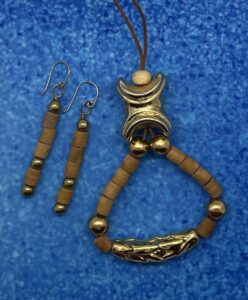 Necklace Set- Acrylic Bead Accent. Gold Metal Cluster Bead. Gold Metal Balls. Wood Barrel Beads. Carved Leaf Gold Metal Pendant. Leather Strung. Approx. length: 20 inches. 3 inch Earrings to Match. 14K Gold Filled Earwire. Pronounced: oo-NAH-edo Origin: Ibo Meaning: Gold